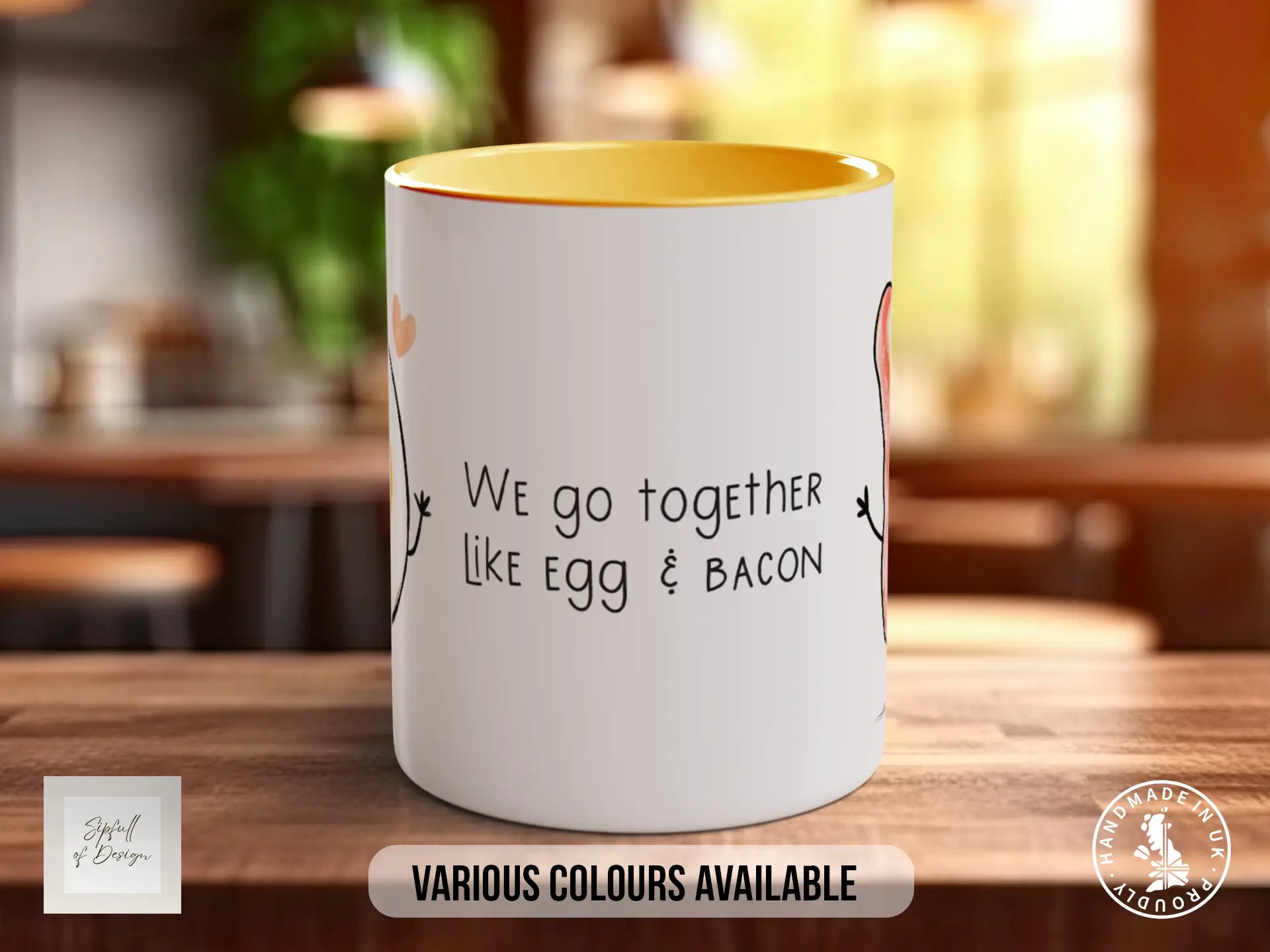 A white mug with a yellow interior, featuring a humorous text that reads "We go together like egg & bacon". The mug is placed on a wooden surface, and there is a blurred background that appears to be a kitchen or dining area.