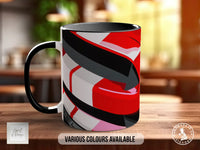 A colorful mug with abstract geometric patterns in red, black, and white sits on a wooden surface.