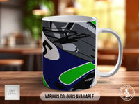 A white ceramic mug with a colorful abstract design featuring shades of blue, green, and gray.