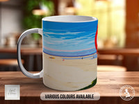 A white mug with a beach scene printed on it, sitting on a wooden surface.