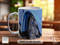 A white ceramic mug with a blue and silver design depicting a car wheel, placed on a wooden surface.
