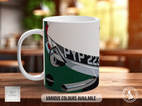 A white mug with a graphic design featuring a motorcycle or scooter on the side, placed on a wooden surface.