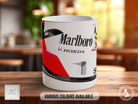 A white ceramic mug with a design featuring a motorcycle helmet and the Marlboro logo, along with the text "Marlboro H Honda" and "S1". The mug is placed on a wooden surface, and there is a blurred background that appears to be a kitchen or dining area.