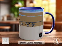 A white and blue mug with a beach scene printed on it, sitting on a wooden surface.