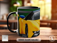 A black and white mug with a colorful illustration of a yellow sports car on it, placed on a wooden surface.
