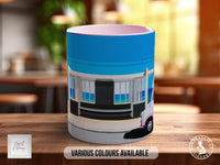 A mug with a colorful illustration of a building on it, placed on a wooden surface.