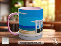 A mug with a colorful design featuring a beach scene, with a blue sky, ocean, and a building in the background.