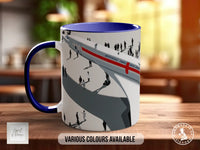 A white mug with a blue rim, featuring an illustration of people on a train.
