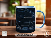 A blue and white mug with a black and white line drawing of a vehicle on it, placed on a wooden surface.