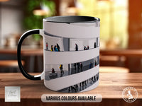 A black and white mug with a graphic design depicting a group of people walking through a hallway or corridor.
