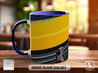 A colorful mug with a yellow and black design, featuring a graphic of a person riding a motorcycle. The mug is placed on a wooden surface, and there is text indicating that various colors are available.