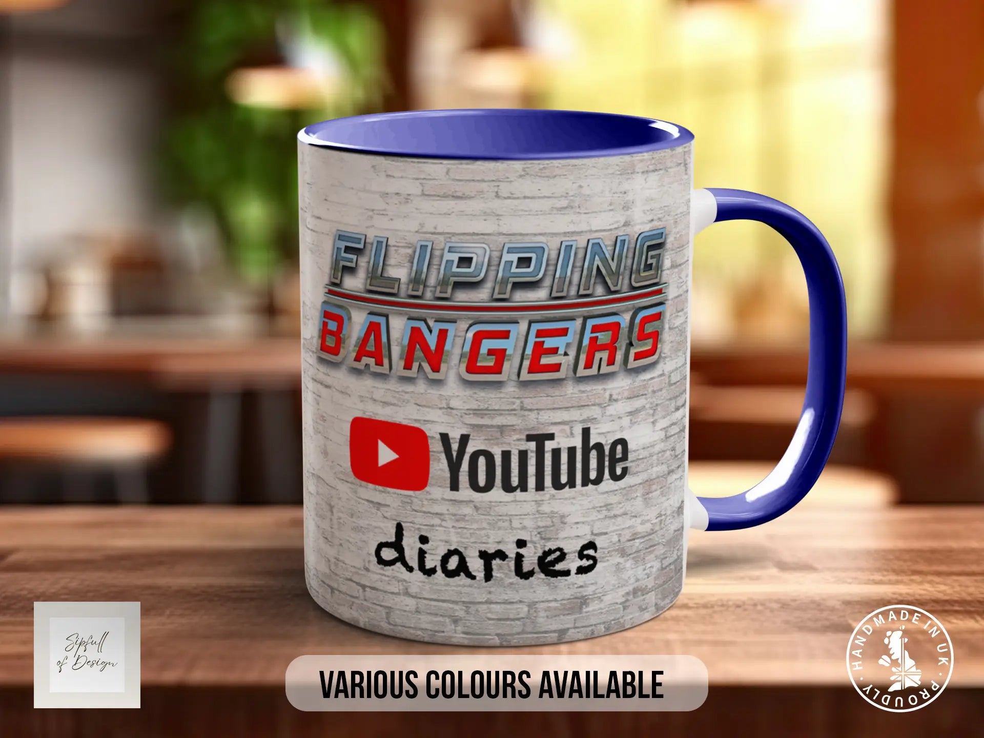 A mug with the text "FLIPPING BANGERS" and "YouTube diaries" printed on it, along with a YouTube logo. The mug is placed on a wooden surface, and there is a blurred background that appears to be a kitchen or dining area.