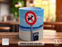 A mug with a beach scene and a red and white no-dog sign on it, placed on a wooden surface.