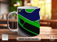 A white mug with a colorful abstract design featuring green, blue, and black colors.