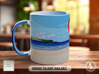 A blue and white mug with a beach scene printed on it, sitting on a wooden surface.