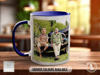 A mug with a printed photo of two people sitting on a bench in a natural setting, with the mug having a blue rim and a white interior.