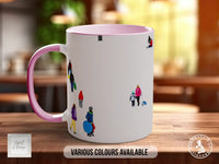 A white mug with a pink interior and various colorful illustrations of people on it, placed on a wooden surface.