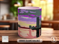 A colorful mug with a cityscape design on it, sitting on a wooden surface.