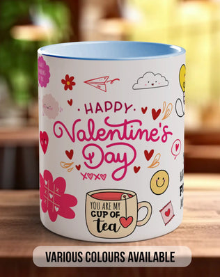 A white mug with a colorful design featuring various Valentine's Day-themed elements such as hearts, flowers, and a cup of tea.
