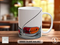 A white ceramic mug with a graphic design depicting a car's headlight on a wooden surface.