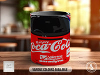 A red Coca-Cola mug with the text "Enjoy Coca-Cola" printed on it, sitting on a wooden surface.