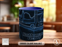 A blue mug with a graphic design featuring a vehicle, likely a car, and the text "Rothmans Rally" printed on it. The mug is placed on a wooden surface, and there is a blurred background that appears to be a kitchen or dining area.