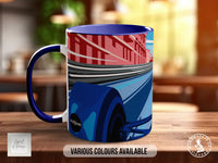 A blue and red mug with a graphic design depicting a car on a road, placed on a wooden surface.