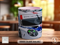 A mug with a racing car design on it, sitting on a wooden surface.