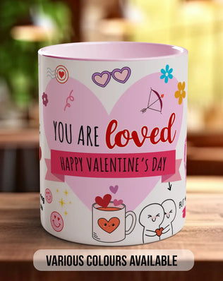 A pink and white mug with a heart-shaped design and various Valentine's Day-themed illustrations, along with the text "YOU ARE LOVED" and "HAPPY VALENTINE'S DAY".