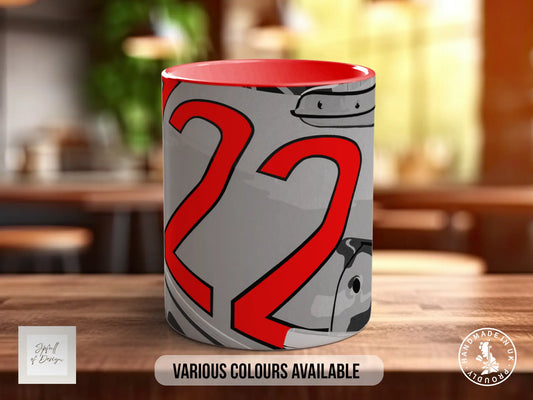 A mug with a red and gray design featuring the number 22, placed on a wooden surface.