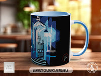 A mug with a blue and black design featuring a gate and a building, placed on a wooden surface.
