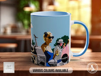 A blue and white mug with an illustration of a woman in sunglasses and a hat, along with other people and objects, on a wooden surface.