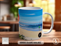 A white ceramic mug with a colorful beach scene printed on it, placed on a wooden surface.
