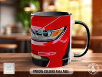 A red mug with a graphic of a car's headlight on it, placed on a wooden surface.