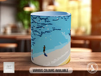 A ceramic mug with a blue and white design depicting a person walking on a beach.