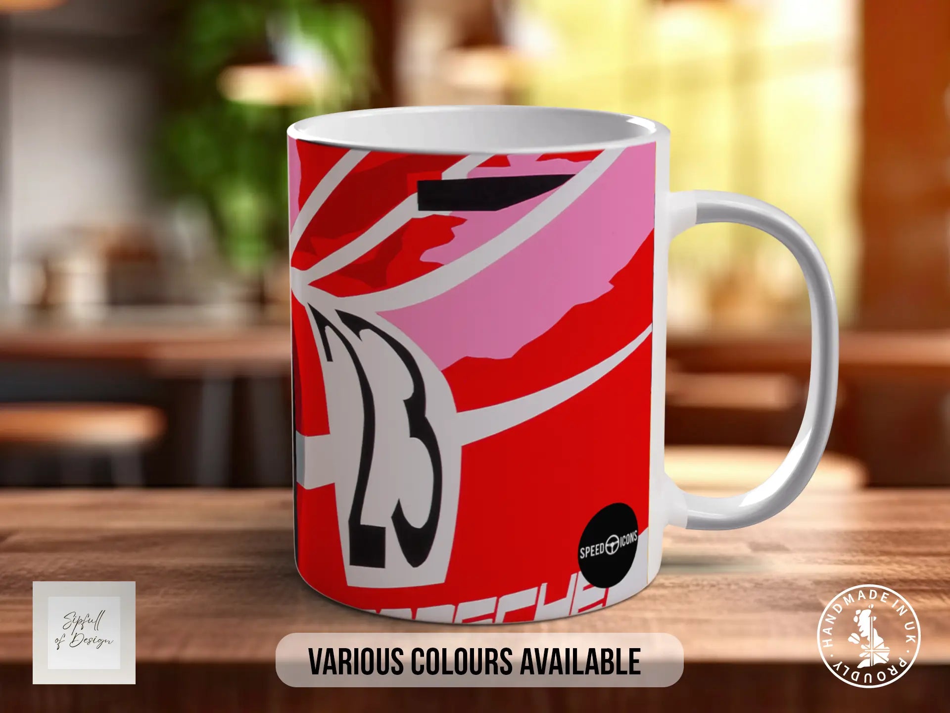 A white ceramic mug with a vibrant red and pink abstract design, featuring the number 23 prominently displayed. The mug is placed on a wooden surface, and there is text indicating that various colors are available.