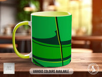 A green and yellow mug with a black and yellow abstract design on it, placed on a wooden surface.