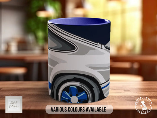 A mug with a graphic design featuring a car and a blue rim, placed on a wooden surface.