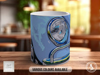 A mug with a blue and white design featuring a car headlight and chrome accents, placed on a wooden surface.