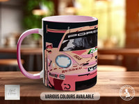 A pink and black mug with a racing car design on it, sitting on a wooden surface.