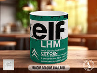 A mug with the word "ELF" printed on it, along with the text "LHM" and "CITROEN" printed below. The mug is placed on a wooden surface, and there is a blurred background that appears to be a kitchen or dining area.