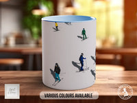 A white mug with a design of people skiing on a snowy slope, featuring various colors.