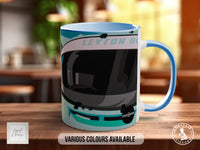 A blue and white mug with a graphic design featuring a car or vehicle. The mug is placed on a wooden surface, and there is text indicating that various colors are available.