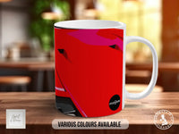 A white ceramic mug with a vibrant red and pink abstract design on it, placed on a wooden surface.