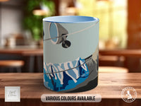 A ceramic mug with a colorful design featuring mountains and a bird, placed on a wooden surface.